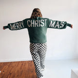 Person wearing a sweater with 'Merry Christmas' text in a minimal indoor setting