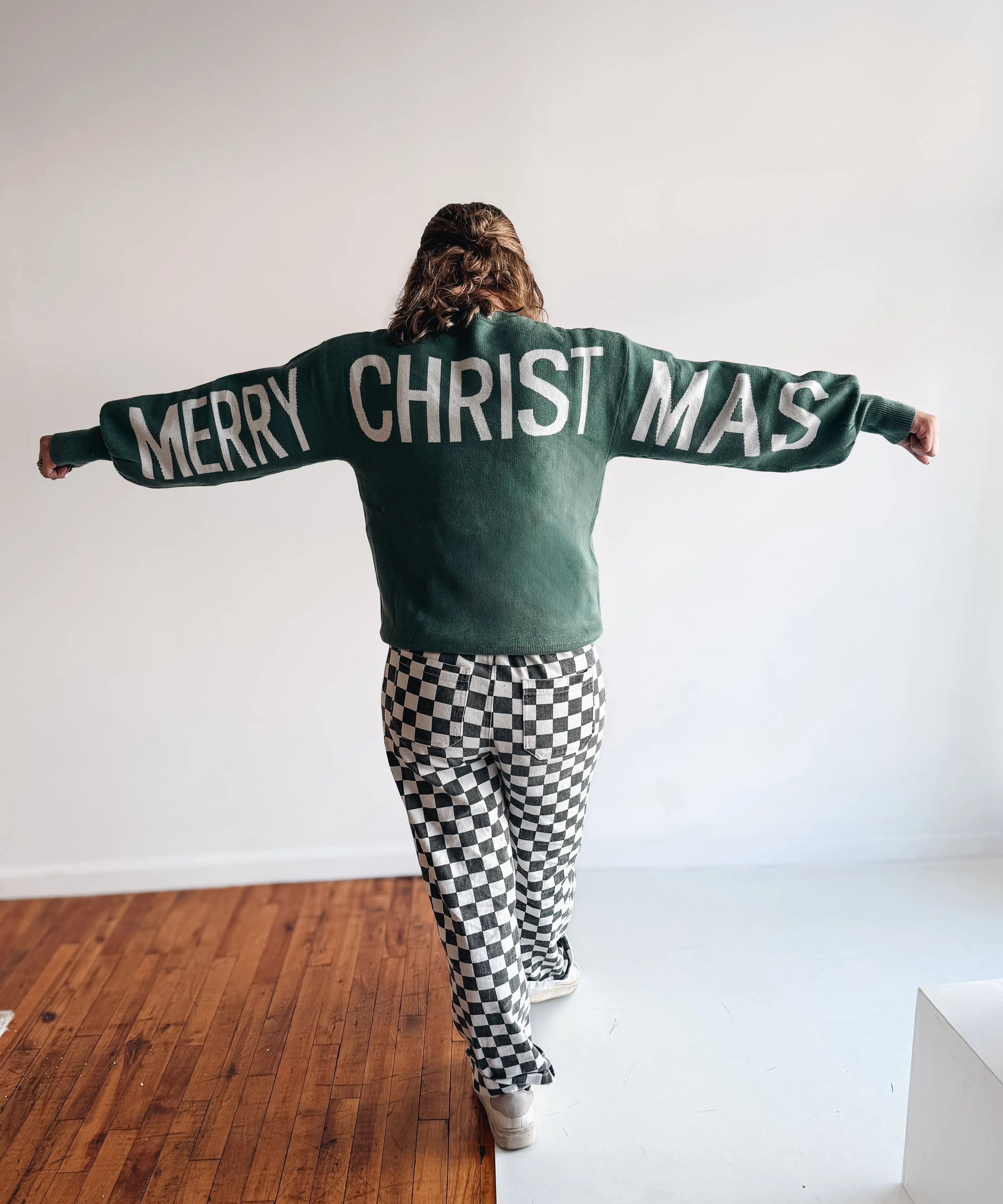 Person wearing a sweater with 'Merry Christmas' text in a minimal indoor setting