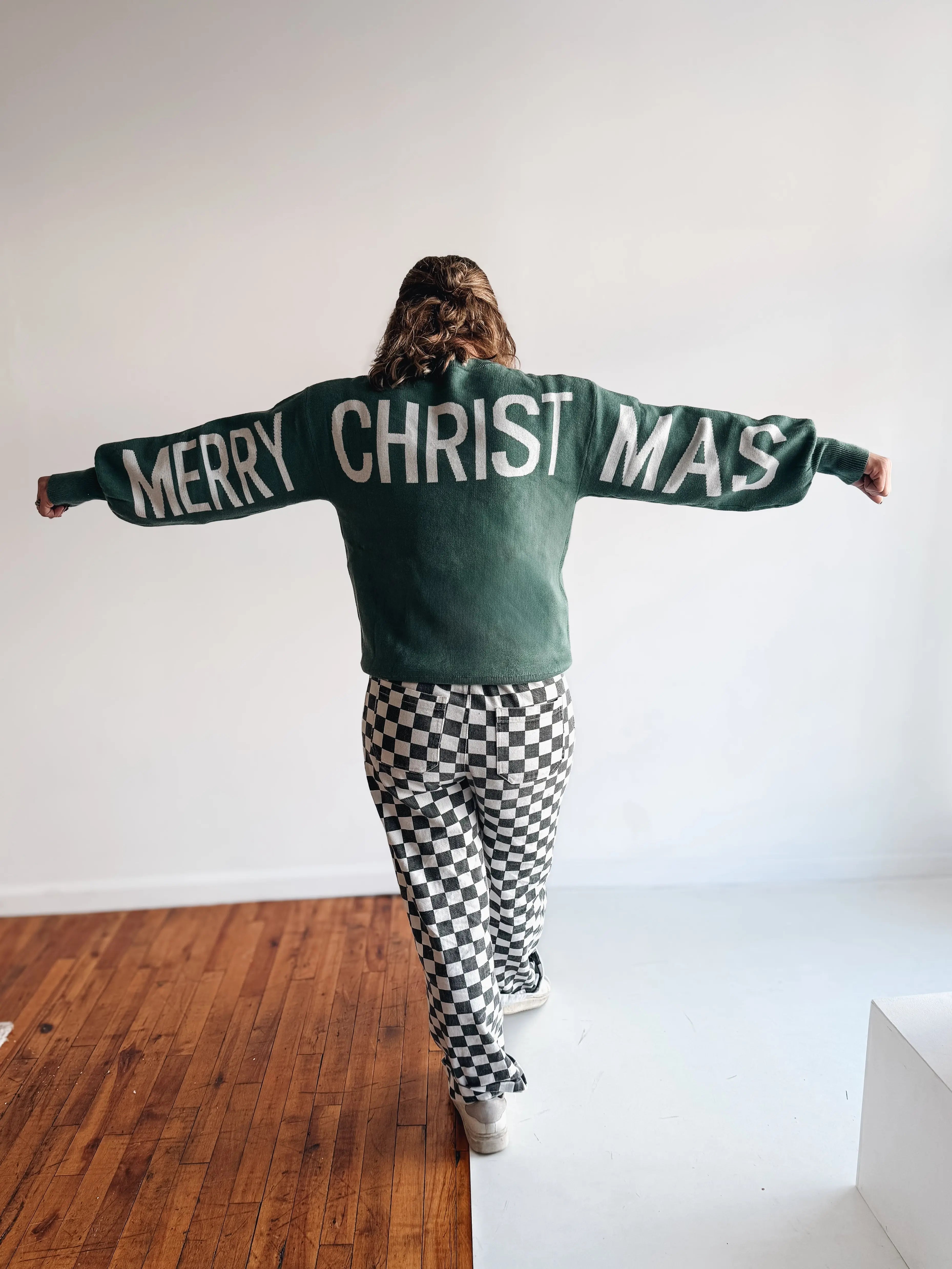 Person wearing a sweater with 'Merry Christmas' text in a minimal indoor setting