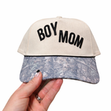 Cap with 'BOY MOM' text held by a hand on a white background