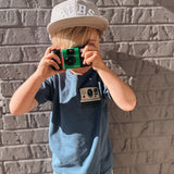 Child holding a vintage camera against a brick wall