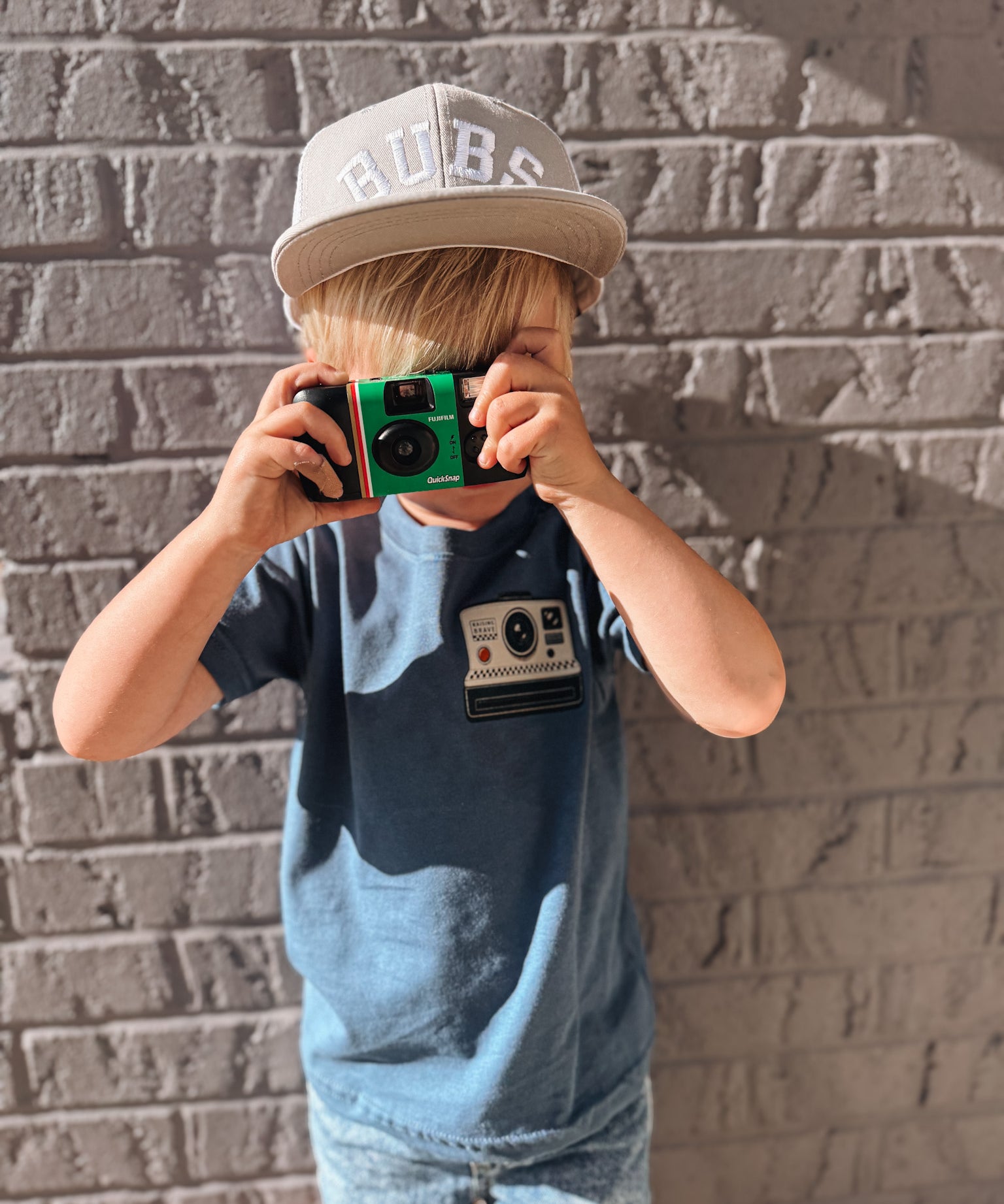 Child holding a vintage camera against a brick wall