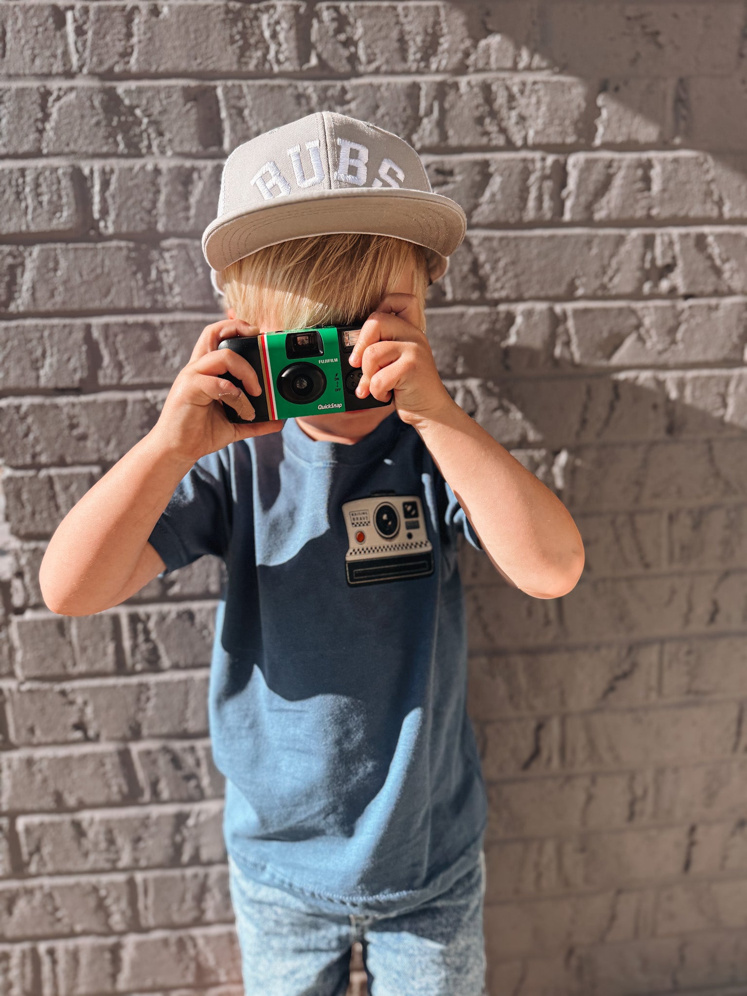 Child holding a vintage camera against a brick wall