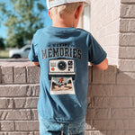 Child wearing a blue t-shirt with 'Making Memories' graphic leaning against a brick wall.