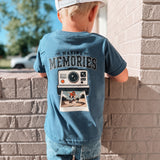 Child wearing a blue t-shirt with 'Making Memories' graphic leaning against a brick wall.
