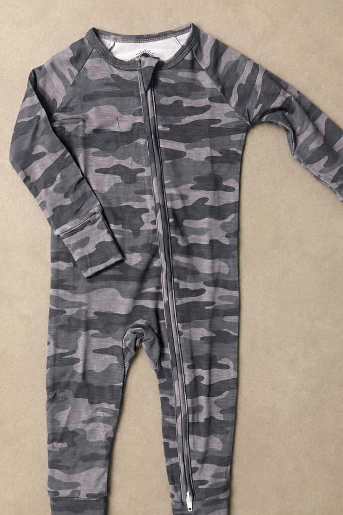 A long-sleeve baby footless one-piece jumpsuit with a gray and black camouflage pattern and a front zipper, laid flat on a textured beige background.