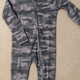 A long-sleeve baby footless one-piece jumpsuit with a gray and black camouflage pattern and a front zipper, laid flat on a textured beige background.