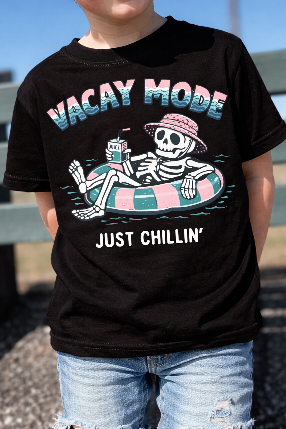 Child wearing a black skeleton vacation tee outside at the park.