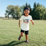 Child wearing a 'All American Dude' t-shirt standing out sidel.