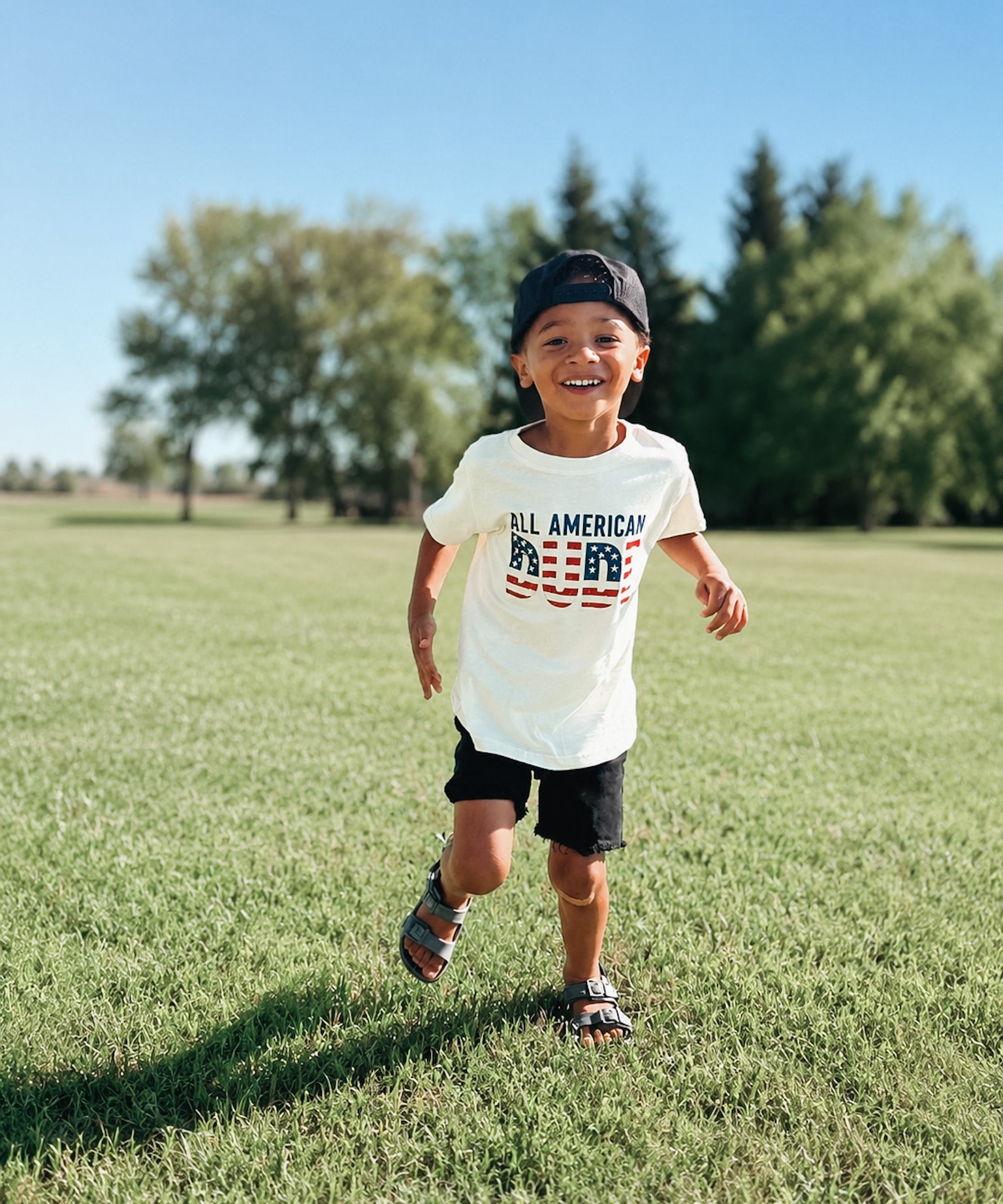 Child wearing a 'All American Dude' t-shirt standing out sidel.