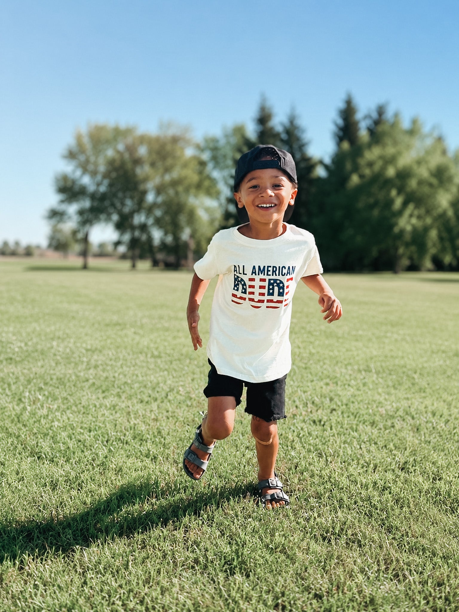 Child wearing a 'All American Dude' t-shirt standing out sidel.