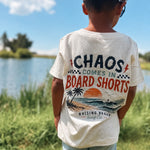 Child wearing a t-shirt with a graphic design and text, standing outdoors near a body of water.