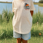 Child wearing a 'Chaos Surf Co' t-shirt outdoors by a lake