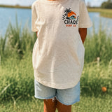 Child wearing a 'Chaos Surf Co' t-shirt outdoors by a lake