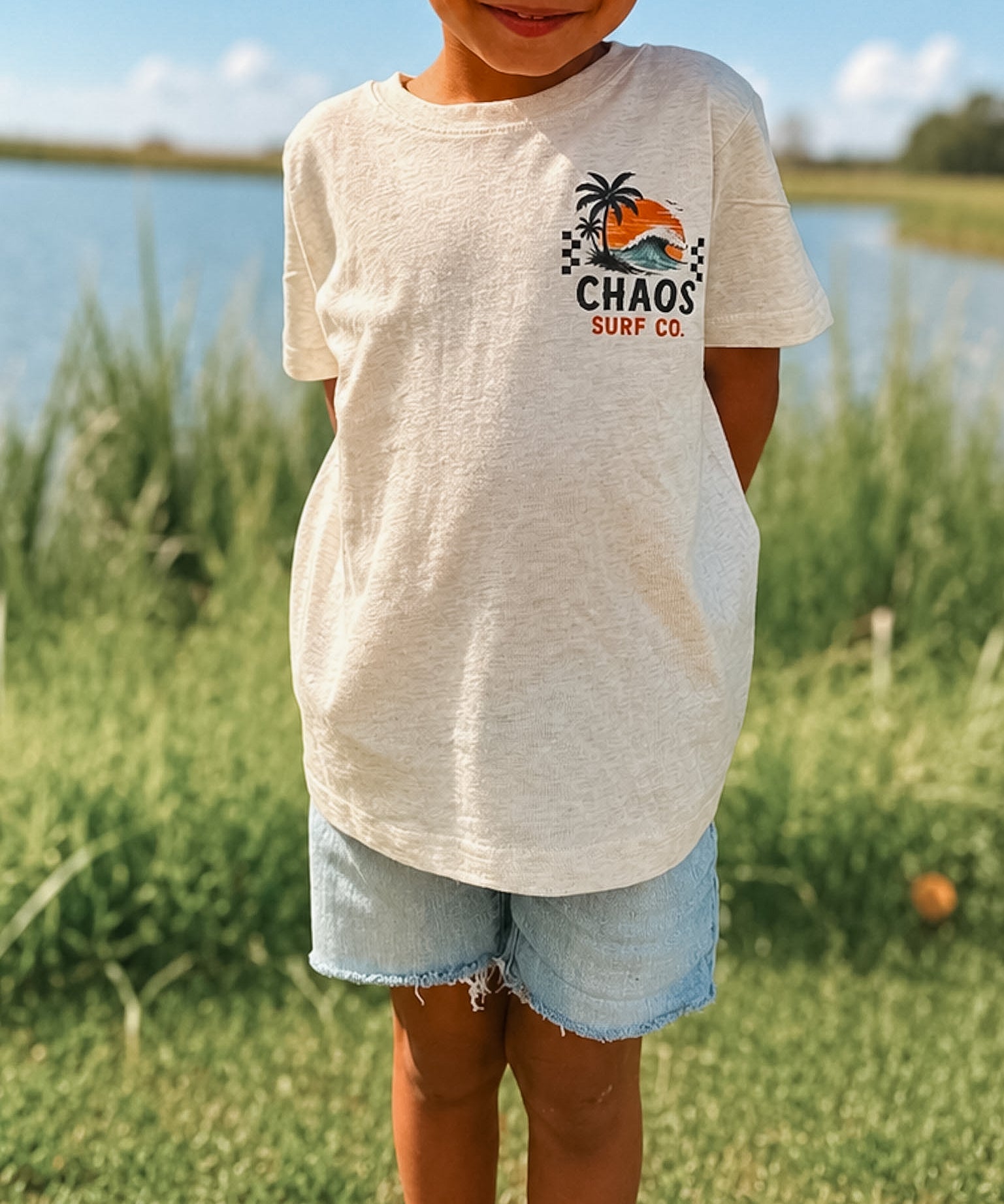 Child wearing a 'Chaos Surf Co' t-shirt outdoors by a lake