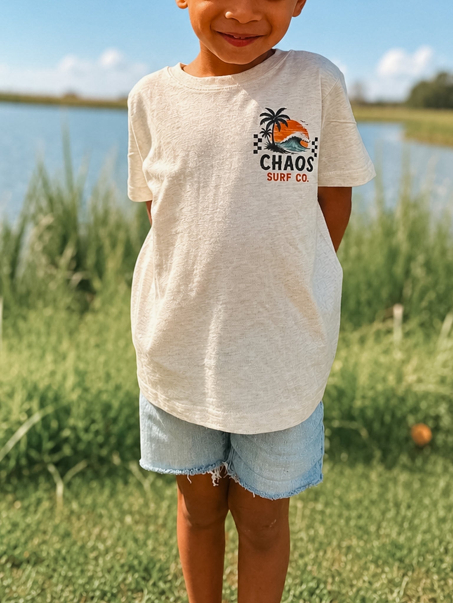 Child wearing a 'Chaos Surf Co' t-shirt outdoors by a lake