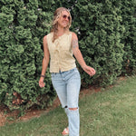Woman in a yellow top and light blue jeans standing in front of a green bush