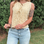 Woman wearing a yellow sleeveless top and blue jeans outdoors.