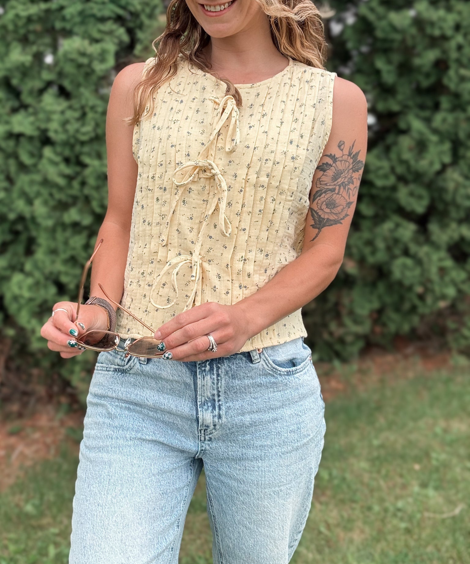 Woman wearing a yellow sleeveless top and blue jeans outdoors.