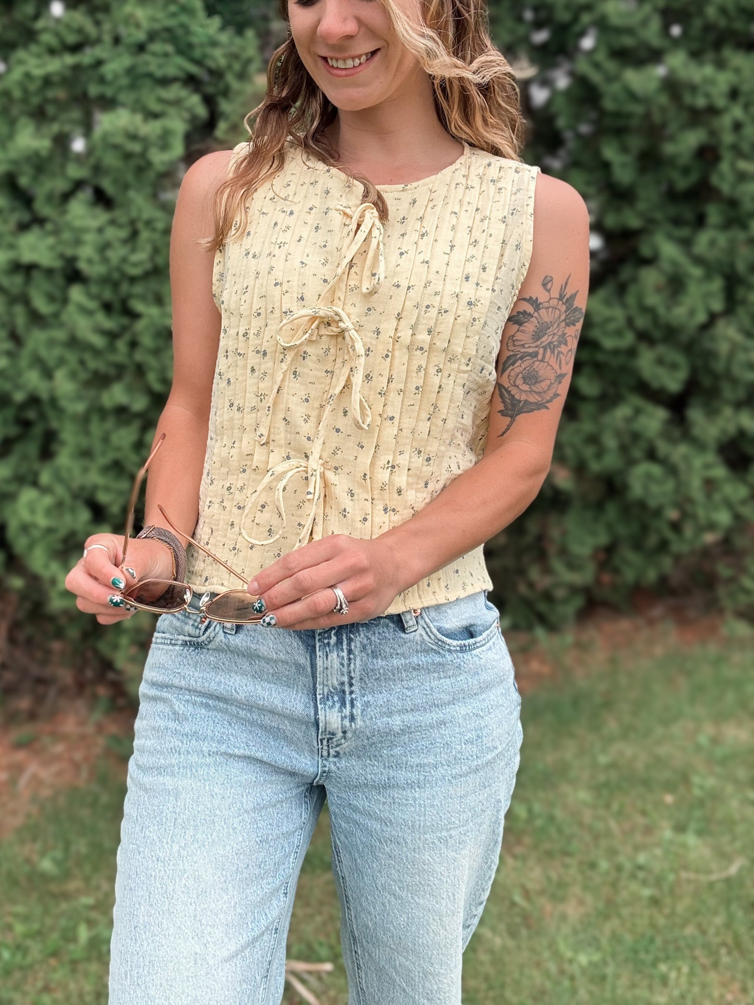 Woman wearing a yellow sleeveless top and blue jeans outdoors.