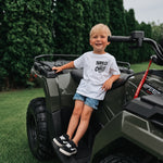 Child sitting on a green ATV with trees in the background