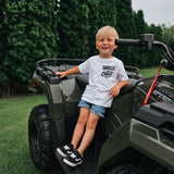 Child sitting on a green ATV with trees in the background