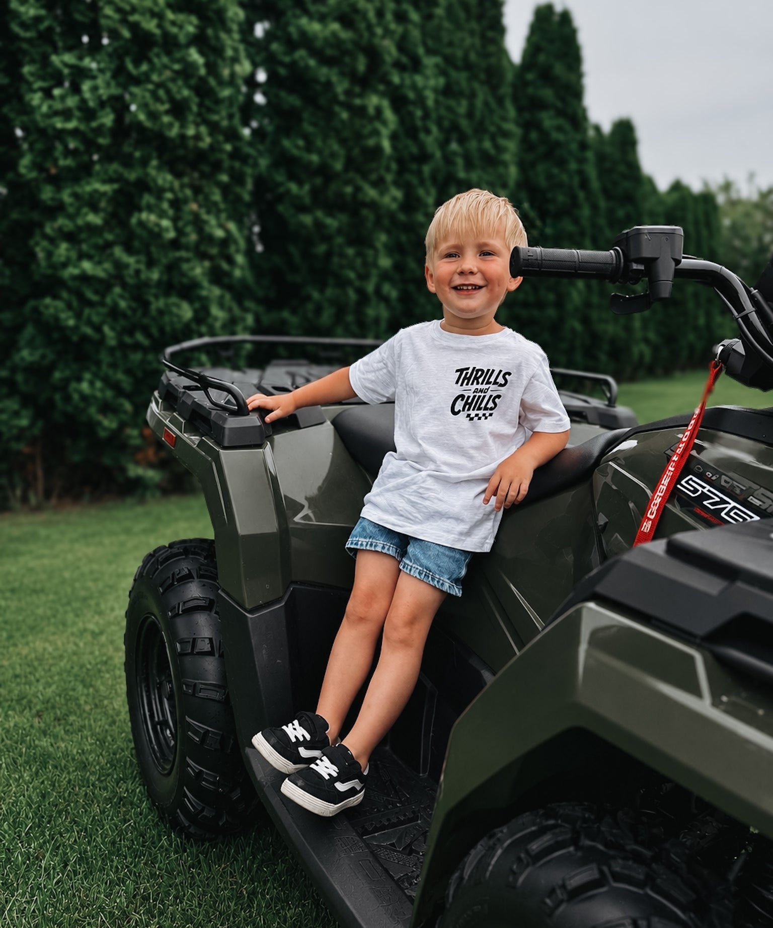 Child sitting on a green ATV with trees in the background