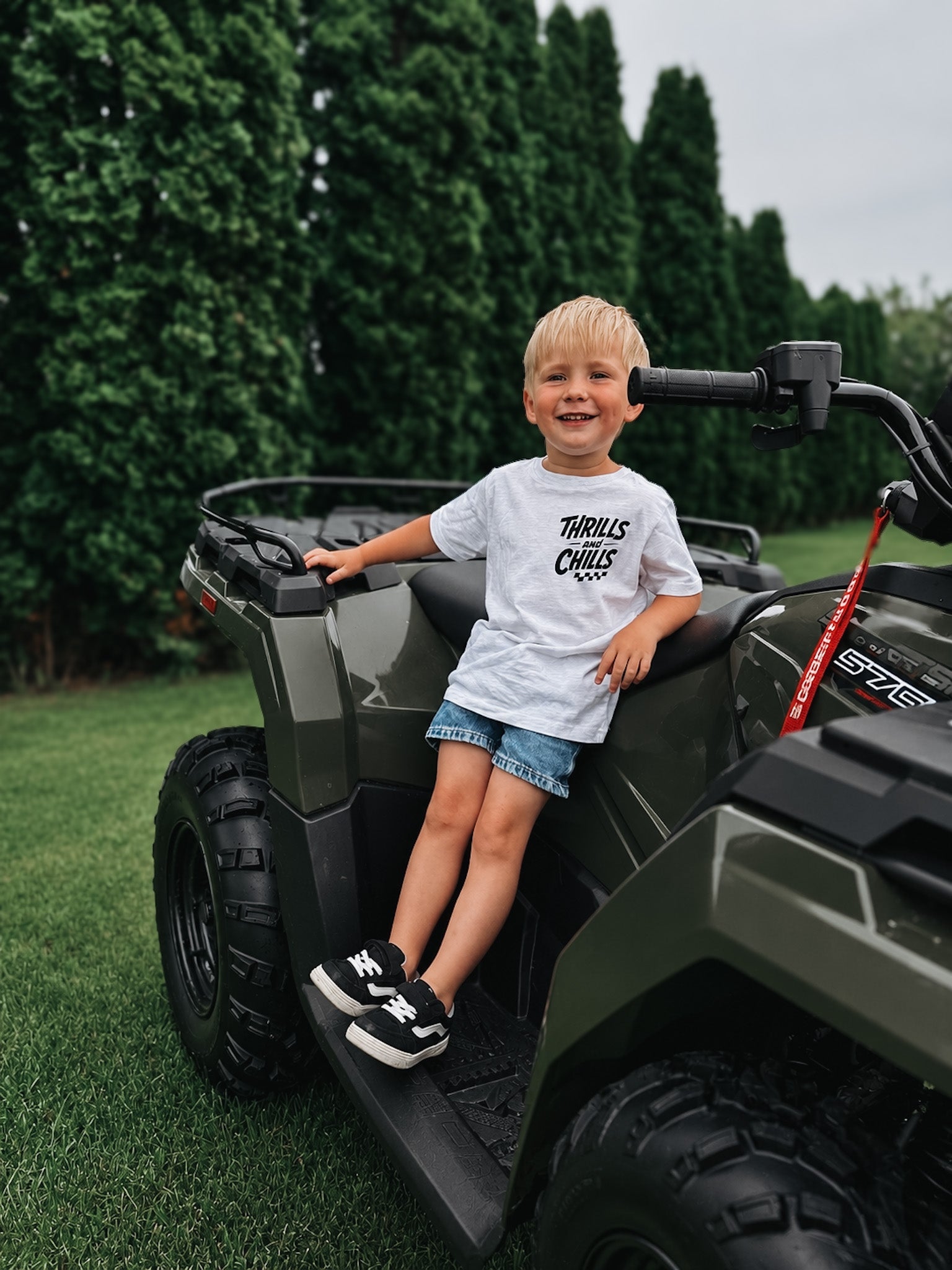 Child sitting on a green ATV with trees in the background