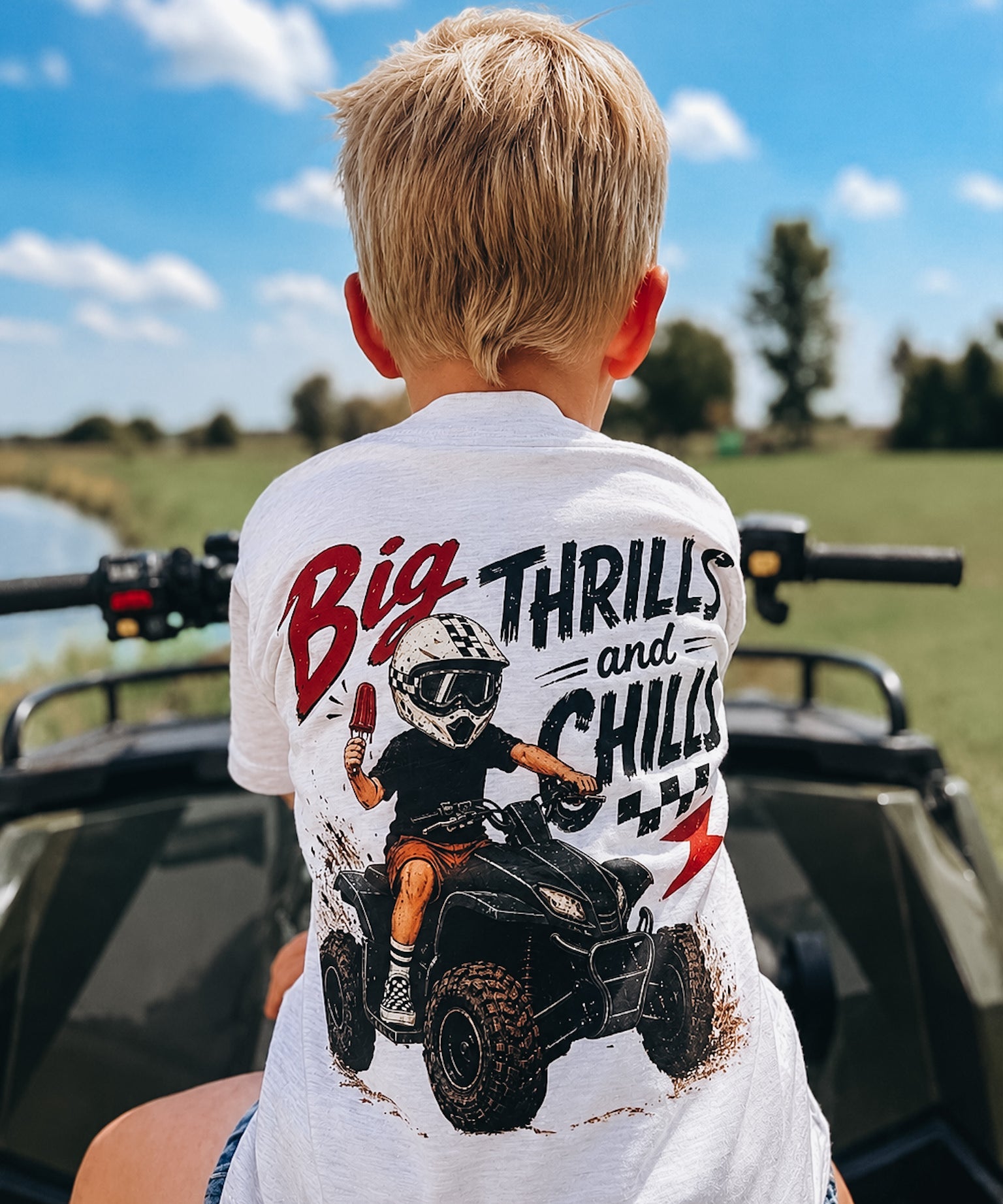 Child wearing a shirt with an ATV graphic and text, sitting on a four-wheeler outdoors.