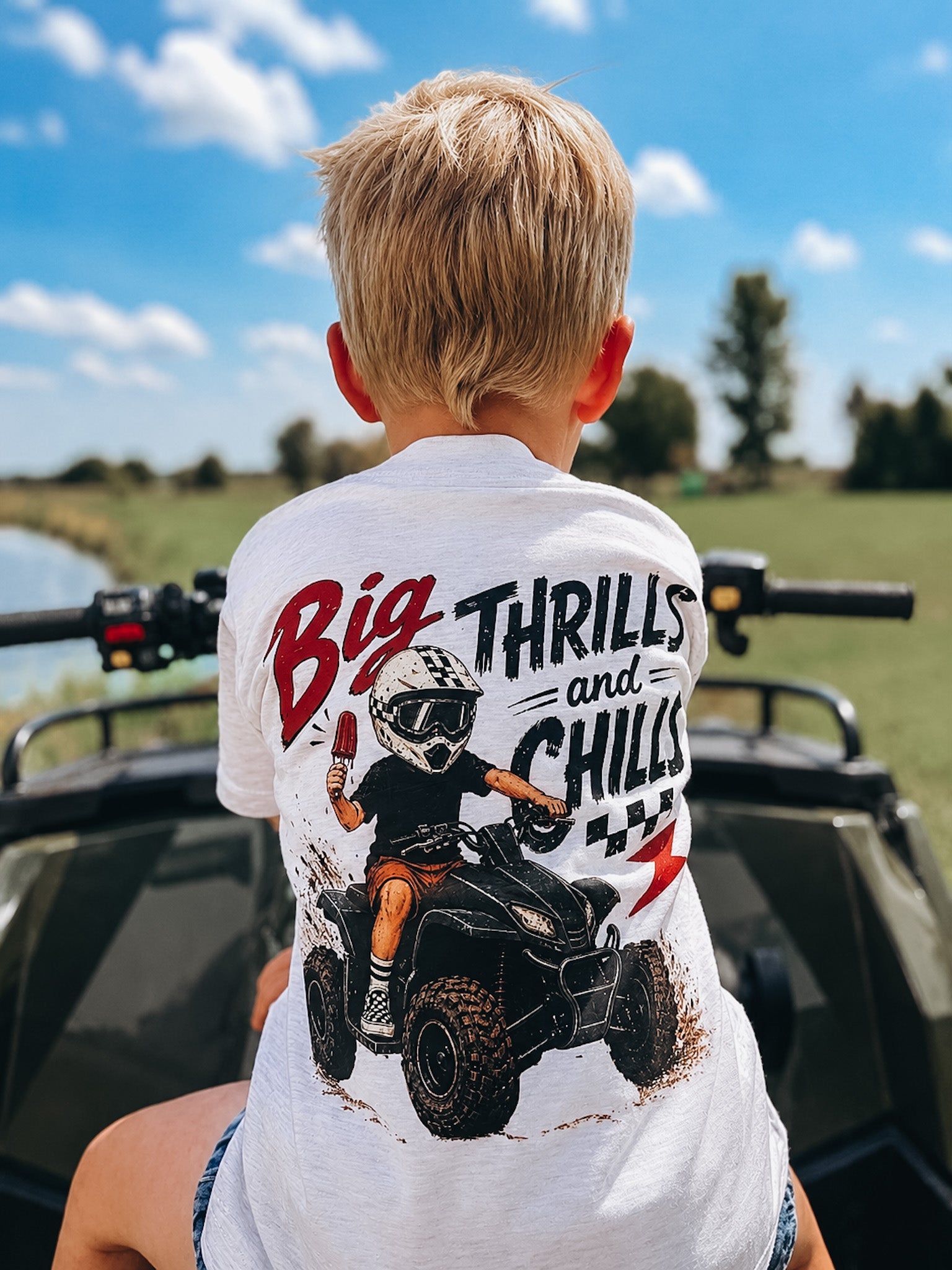 Child wearing a shirt with an ATV graphic and text, sitting on a four-wheeler outdoors.