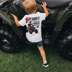 Child wearing a t-shirt with an ATV graphic standing next to a four-wheeler on grass