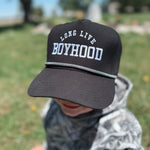 Child wearing a black cap with 'Long Live Boyhood' text in a park setting