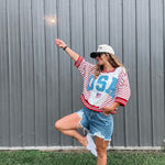 Person wearing a 'USA' themed outfit with a sparkler against a gray wall.