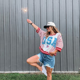 Person wearing a 'USA' themed outfit with a sparkler against a gray wall.