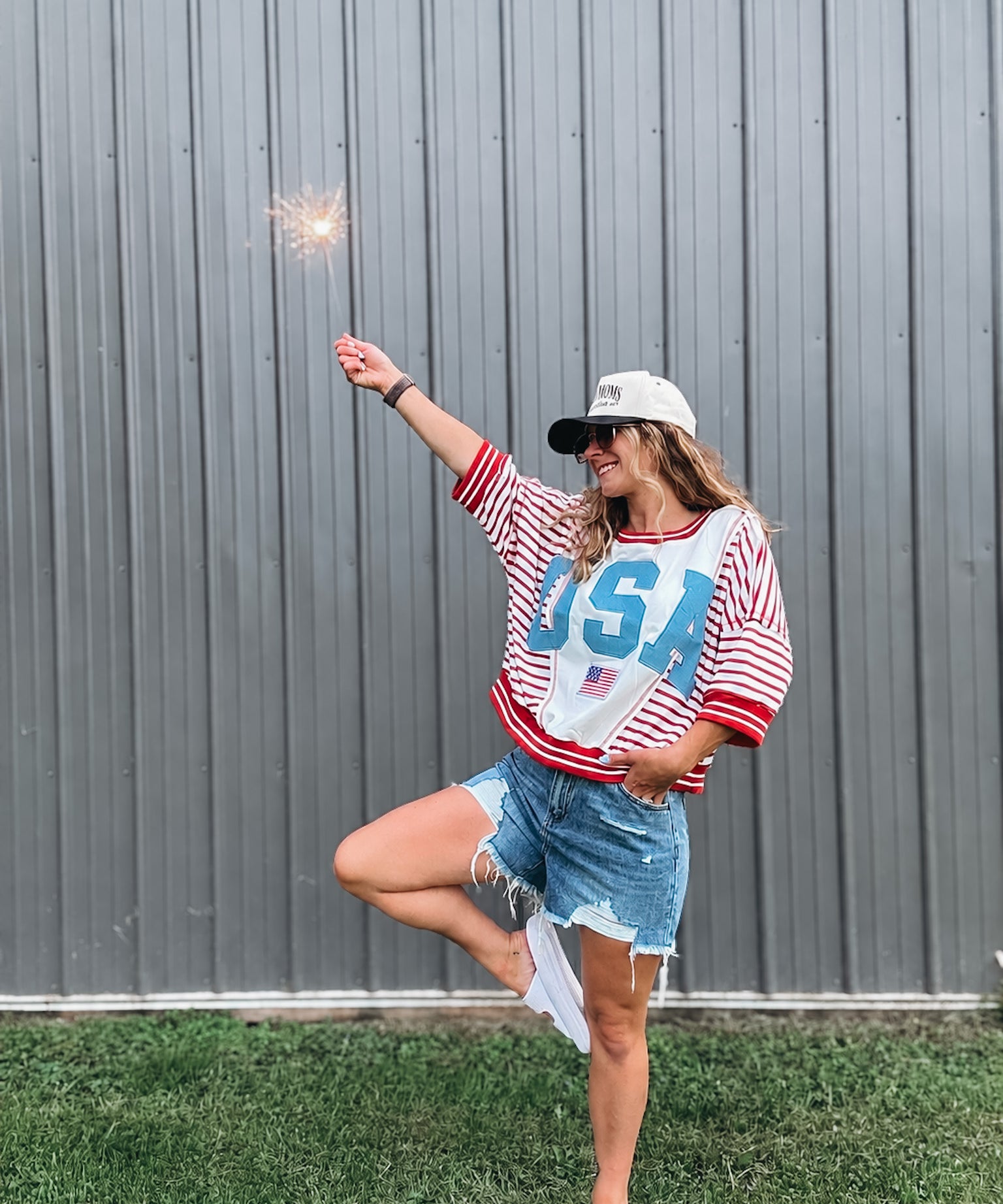 Person wearing a 'USA' themed outfit with a sparkler against a gray wall.
