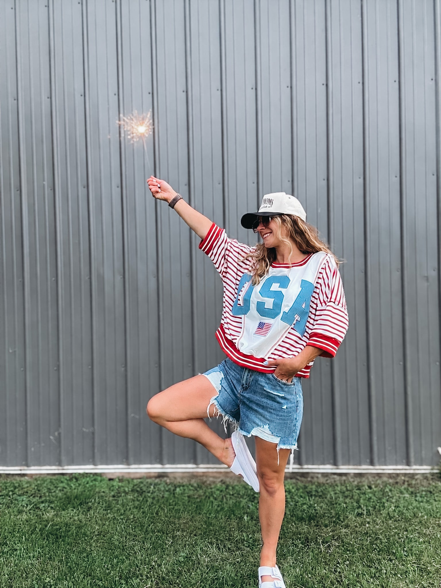 Person wearing a 'USA' themed outfit with a sparkler against a gray wall.