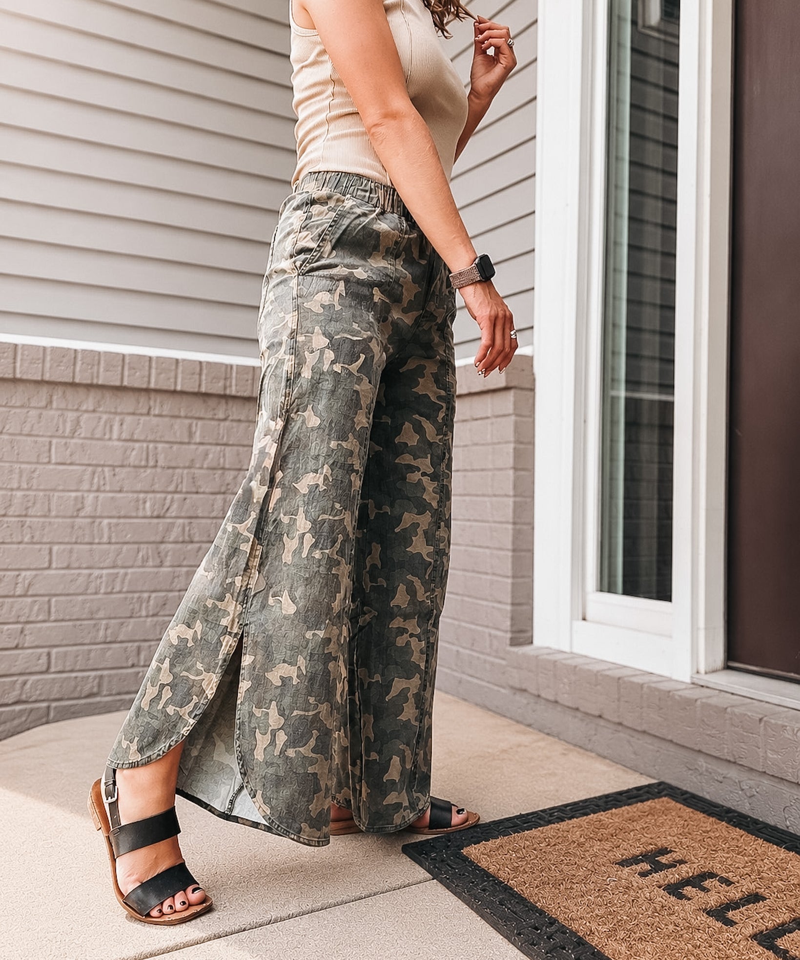 Person wearing camouflage pants standing on a porch with a 'HELLO' doormat.