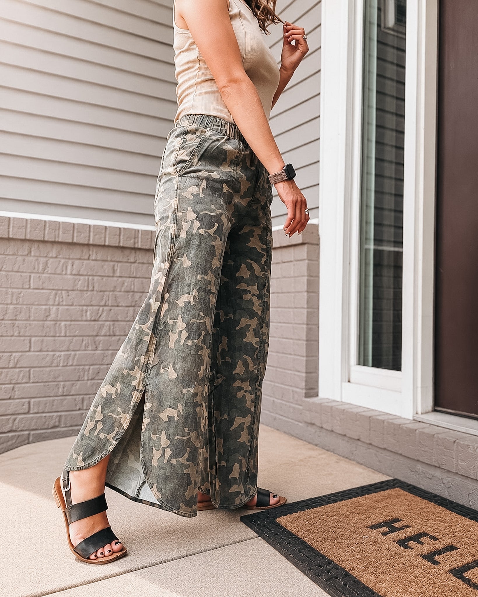 Person wearing camouflage pants standing on a porch with a 'HELLO' doormat.