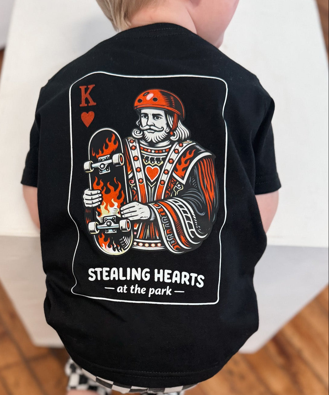 Child wearing a black t-shirt with a graphic design on a wooden floor.