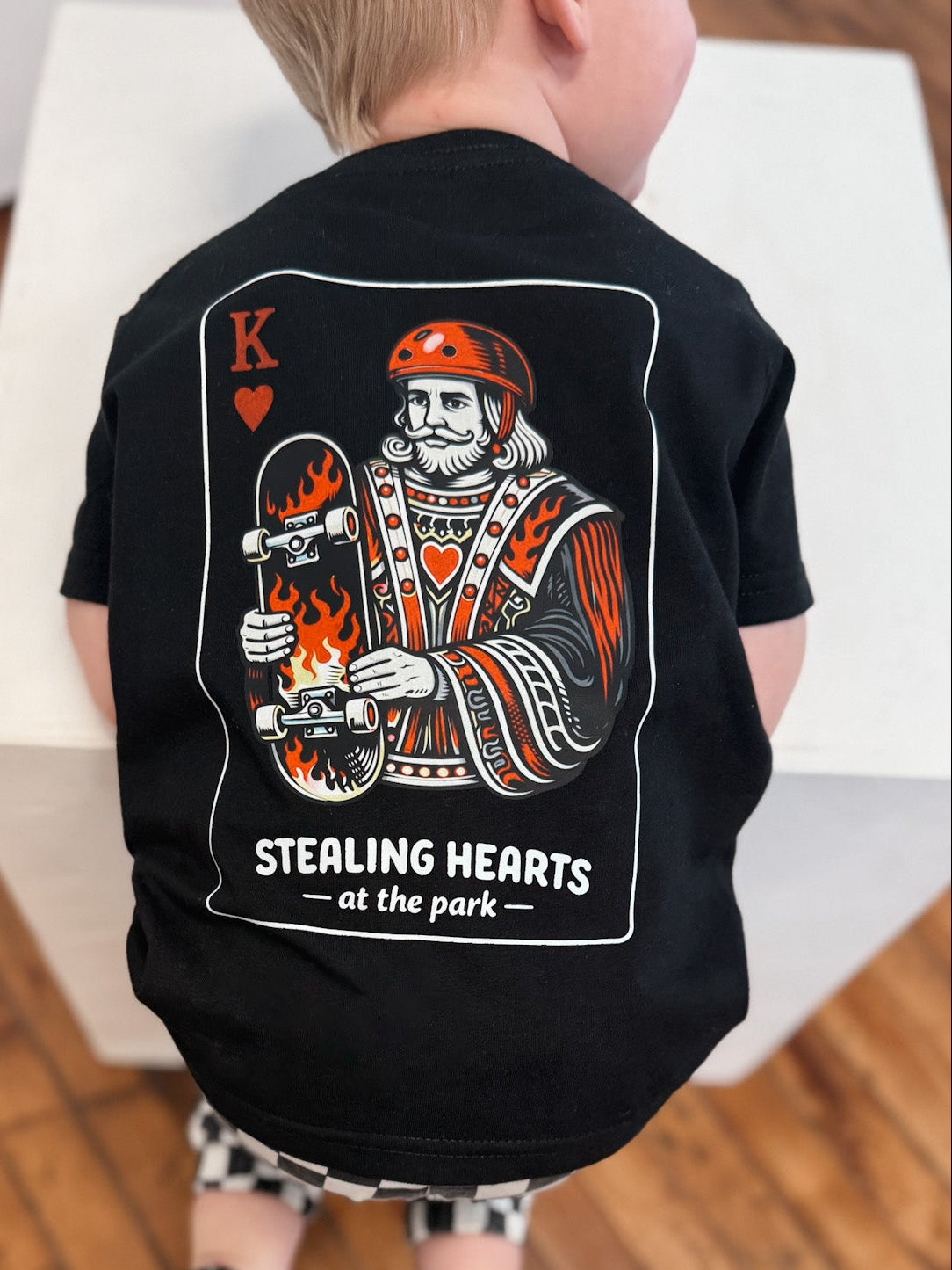 Child wearing a black t-shirt with a graphic design on a wooden floor.