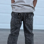 Child wearing a light gray sleeveless hoodie and dark jeans standing in front of a white garage door.