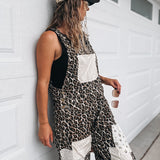 A woman wearing a black and brown leopard print overall jumpsuit with white patch pockets, a beige baseball cap, and sunglasses, leaning against a white garage door.
