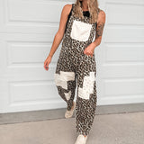 A woman wearing a sleeveless leopard-print overall jumpsuit with white patch pockets, a white baseball cap, and white sneakers, standing in front of a white garage door.