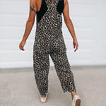 A woman wearing a sleeveless leopard-print jumpsuit with black shoulder panels, shown from behind as she walks on a light gray concrete surface.