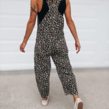 A woman wearing a sleeveless leopard-print jumpsuit with black shoulder panels, shown from behind as she walks on a light gray concrete surface.