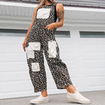 A woman wearing a black and white leopard-print sleeveless jumpsuit with white patch pockets, styled with a white cap, black visor, and white slip-on sneakers, standing in front of a white garage door.