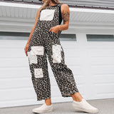 A woman wearing a black and white leopard-print sleeveless jumpsuit with white patch pockets, styled with a white cap, black visor, and white slip-on sneakers, standing in front of a white garage door.
