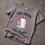 A short-sleeve crewneck t-shirt in a washed, heathered dark gray or charcoal color, laid flat on a textured concrete surface. The shirt features a graphic of a cartoon ghost wearing an orange cap and sunglasses while holding an orange skateboard, with the text 'TOO GHOUL FOR SCHOOL' printed in black arched above and below the illustration.