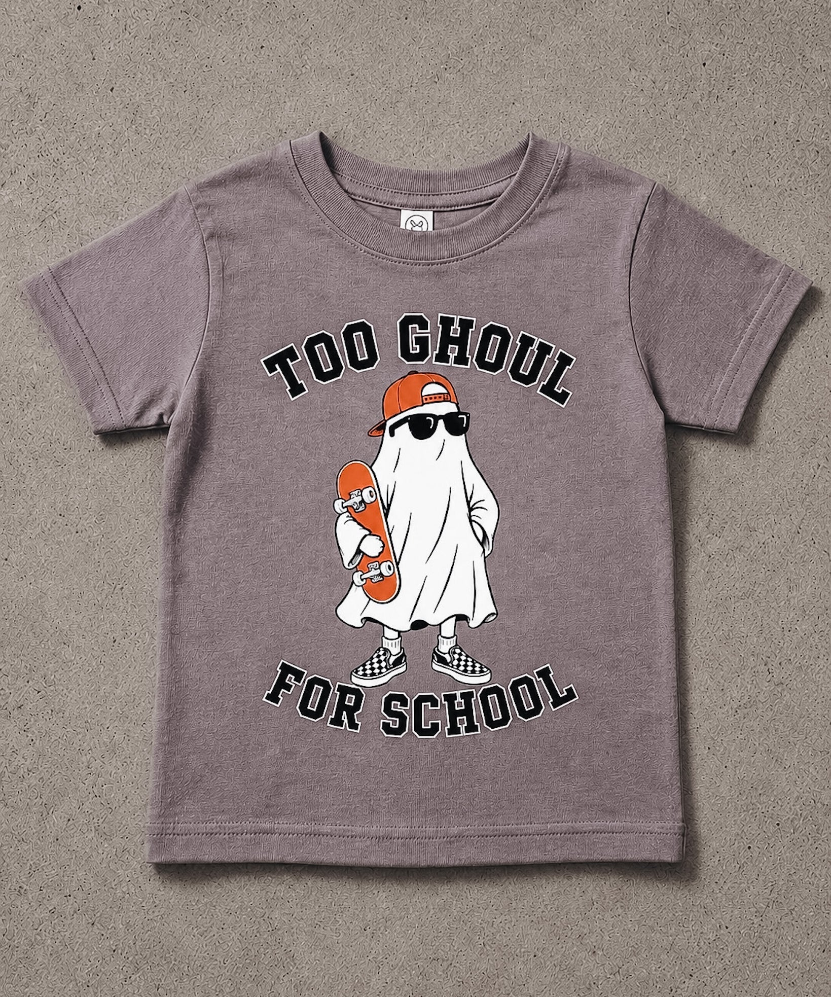 A kids' short-sleeve t-shirt in a washed, heathered mauve-purple color, featuring a cartoon graphic of a ghost dressed as a skateboarder with the text 'TOO GHOUL FOR SCHOOL'. The t-shirt is laid flat on a textured gray concrete surface.