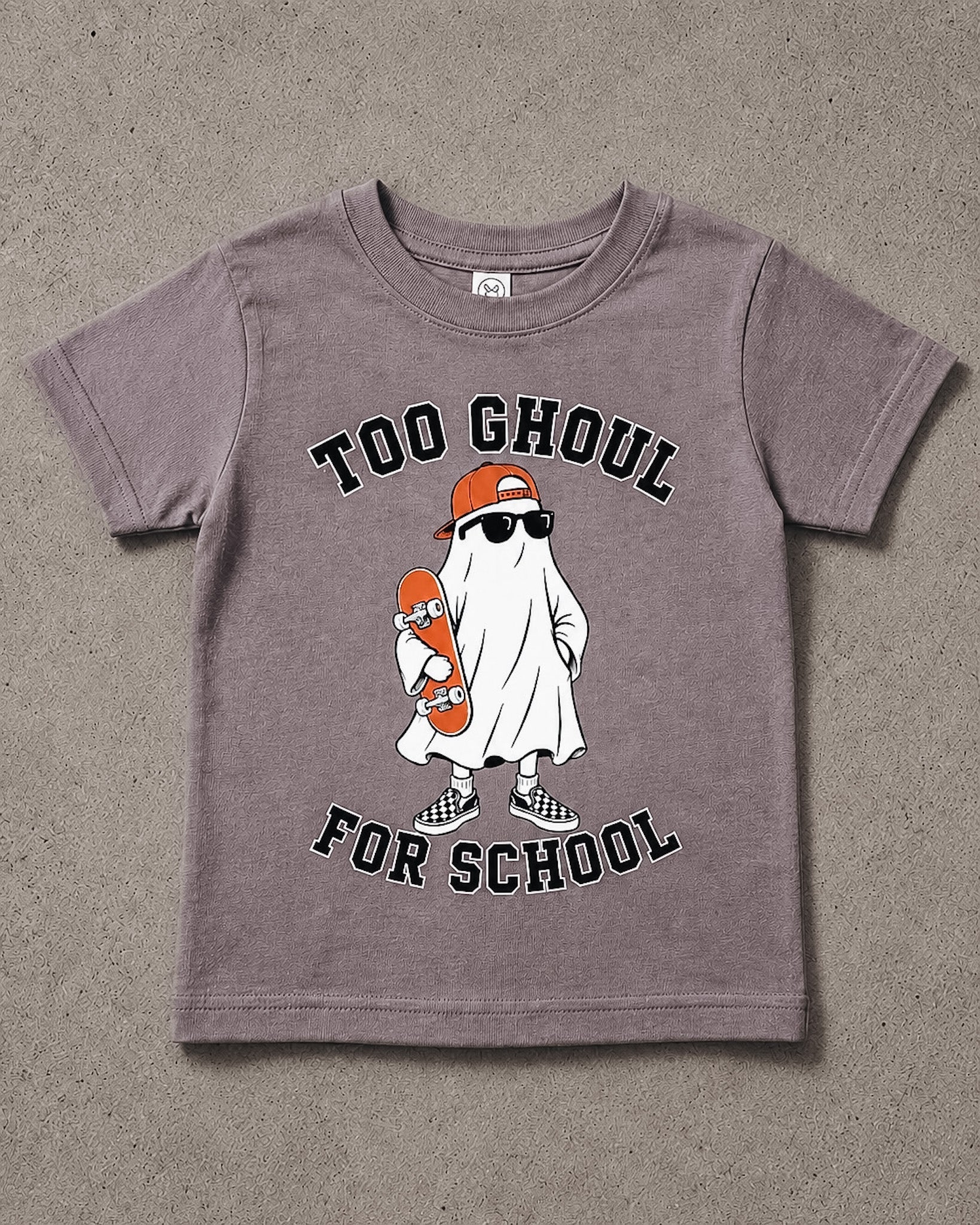 A kids' short-sleeve t-shirt in a washed, heathered mauve-purple color, featuring a cartoon graphic of a ghost dressed as a skateboarder with the text 'TOO GHOUL FOR SCHOOL'. The t-shirt is laid flat on a textured gray concrete surface.